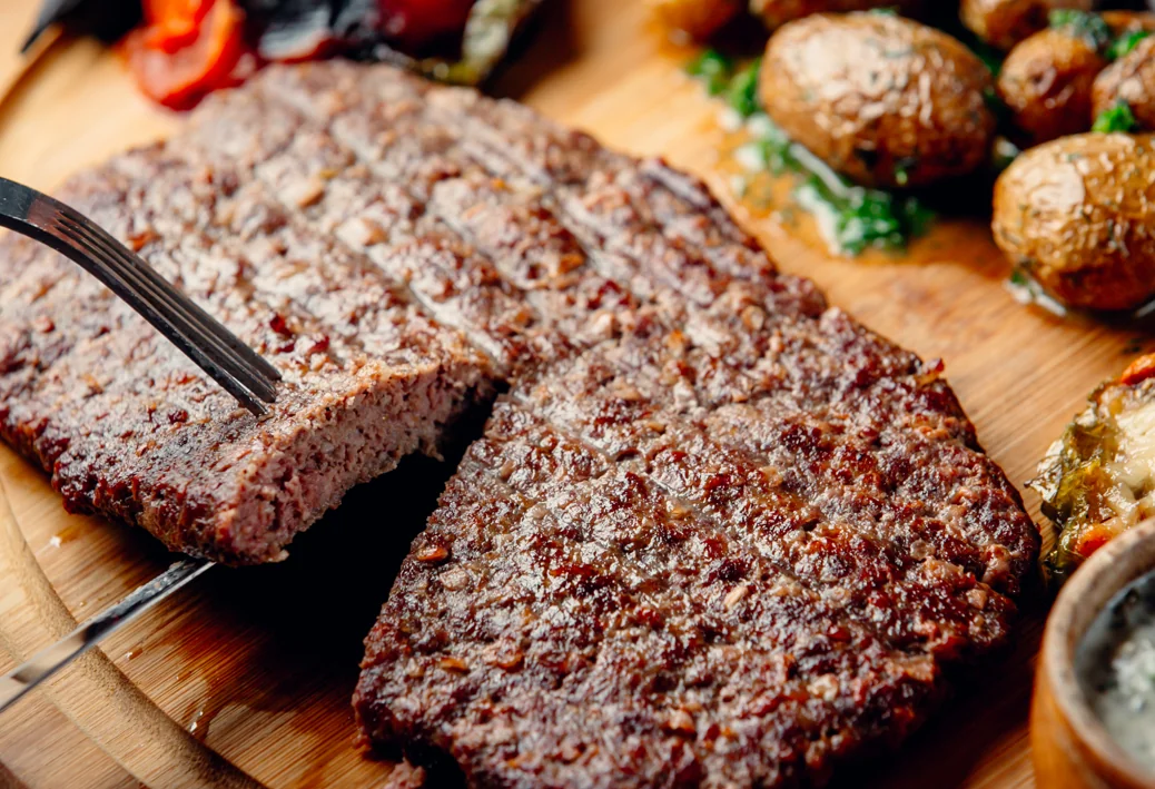 Wide grilled pljeskavica beef patty with a cut section showing the cooked interior